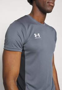 Grå trenings T-skjorte laget av fukttransporterende stoff, med en tettsittende design, korte ermer og en hvit Under Armour-logo på brystet.