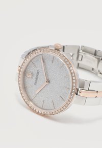 Στρογγυλό ρολόι ασημί και ροζ χρυσού με στεφάνη διακοσμημένη με κρυστάλλους, λαμπερό ασημί καντράν και μεταλλικό μπρασελέ, δείχνει ώρα 10:10.