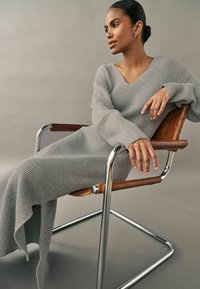 Robe en tricot ribbed gris avec un décolleté en V, des manches longues et un ourlet fluide, associée à une chaise en cuir chromé et marron.