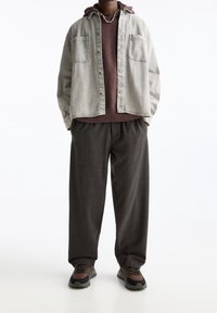 Szara dżinsowa koszula, bordowy sweter dzianinowy, luźne ciemne spodnie i czarno-brązowe sneakersy. Wyraźne szczegóły to dwie przednie kieszenie na koszuli.