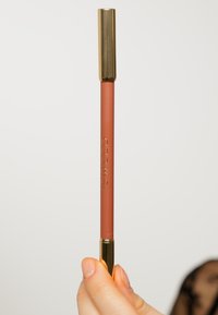 Matita labbra opaca in morbido marrone rossastro, con cappuccio dorato e nome del marchio inciso. Texture liscia, forma cilindrica per una facile impugnatura.