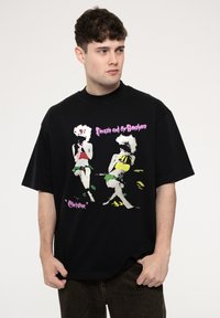 Black oversized t-shirt with a printed graphic depicting two figures in vibrant colors. Features a round neck and short sleeves.