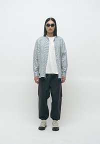 Stripete sølv oversized skjorte, hvit t-skjorte, svarte løse bukser og mørke solbriller. Sneakers har svarte såler med grå detaljer.