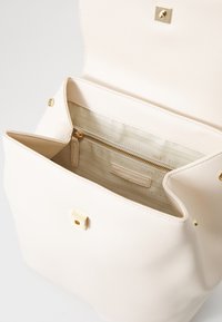 Lichtbeige handtas met een textuur oppervlak, gouden hardware en een veilige drukknoopsluiting. Het interieur heeft een ritszak en is gevoerd.