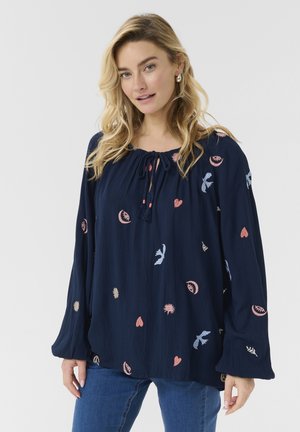 Blouse marine à manches longues, ornée de motifs brodés colorés incluant des cœurs et des oiseaux, avec un col à cordon.