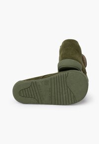 Green suede shoe with a rubber sole featuring textured grip patterns and a Velcro strap. Rounded shape with a soft finish.