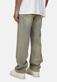 Jeans en denim bleu au design ample, avec des poches arrière, une couleur délavée et des coutures contrastantes. Associés à des baskets blanches.