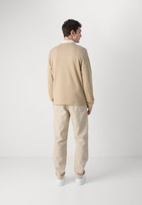 Bluză bej cu mânecă lungă și guler alb, asortată cu pantaloni bej deschis și adidași albi. Design simplu cu o croială lejeră.