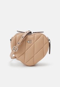 Srdcovitá kabelka z béžové umělé kůže s diamantovým prošíváním, se stříbrnými detaily a odnímatelným nastavitelným popruhem.