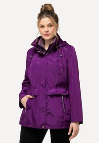 Lila vindjacka med huva, dragsnodd i midjan, fickor med dragkedja och en slät, glänsande yta. Accentuerad med ett mönstrat foder.