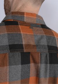 Koszula w kratę w odcieniach szarości, czerni i pomarańczy. Posiada ostro zakończony kołnierz, detale przeszycia oraz małą metkę z logo przy szyi.