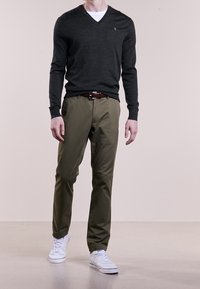 Dunkelgrauer V-Ausschnitt-Pullover, olivgrüne Hose, weiße Sneaker. Besitzt ein kleines Logo auf der Brust, was ein lässiges Outfit schafft.