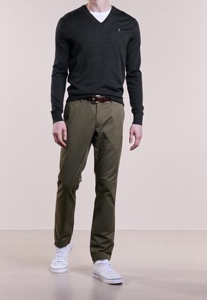 Tummanharmaa V-päähineinen neule, oliivinvihreät housut, valkoiset lenkkarit. Rinnassa on pieni logo, mikä luo rentoa asukokonaisuutta.