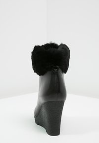 Bottines compensées noires en cuir lisse avec un bord en fausse fourrure noire moelleuse. Talon texturé et détail avec bouton à l'arrière.