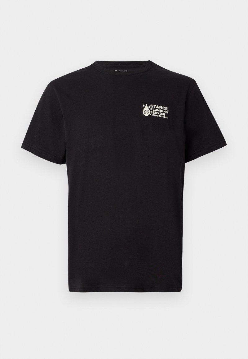 Melnā T-kreklā ar īsām piedurknēm, kuram uz kreisā krūtīm ir neliela balta "Stance Plumbing Service" logo un tālruņa numurs.