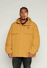 Κίτρινο επενδεδυμένο μπουφάν με κουκούλα, διαθέτει μπροστινό φερμουάρ, δύο υπερυψωμένες τσέπες και ένα μικρό λογότυπο στο στήθος. Υφασμάτινη υφή και άνετη εφαρμογή.