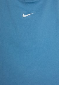 Modra rebrasta tkanina brezrokavnik s centriranim belim logotipom Nike na prsih. Tekstura je gladka in enakomerna.