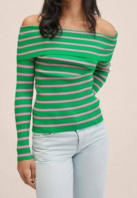 Haut vert côtelé à épaules dénudées avec des rayures roses, manches longues, coupe ajustée et tissu texturé, associé à un jean bleu clair.