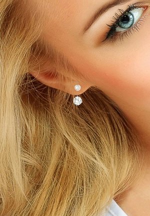 Boucles d'oreilles en argent avec deux cristaux ronds transparents de tailles différentes, présentées dans un design simple, positionnées sur l'oreille d'un modèle.