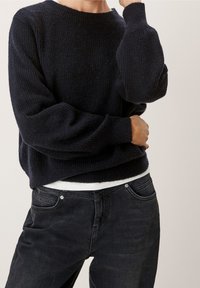 Granatowy sweter dzianinowy o prążkowanej fakturze, okrągłym dekolcie i luźnych rękawach, w połączeniu z ciemnoniebieskimi dżinsami.