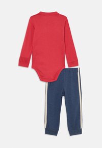 Rød langermet bodysuit kombinert med marineblå bukser som har kremfargede sidestriper. Begge er laget av mykt, elastisk stoff som egner seg for spedbarn.