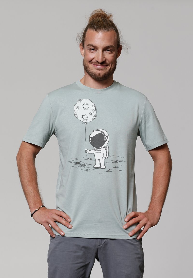 Lichtgroen T-shirt van katoen. Bevat een grafisch ontwerp van een astronaut die een maanvormige ballon vasthoudt in zwart-wit. Korte mouwen.