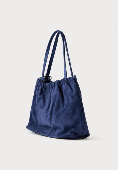 Donkerblauwe suède boodschappentas met samengevouwen bovenkant, twee schouderbanden en een vlakke bodem voor stabiliteit. Zachte textuur met minimale naden.