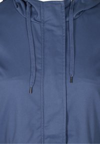 Sinisen hupullisen takin lähikuva, jossa näkyy metalliset nyörinpäät ja etusauman yksityiskohdat kangaspinnassa.