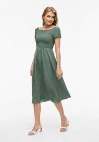 Grön, midilång klänning gjord av lätt tyg. Har en smockad bodice, avtagna axelärmar och en flödande kjol.