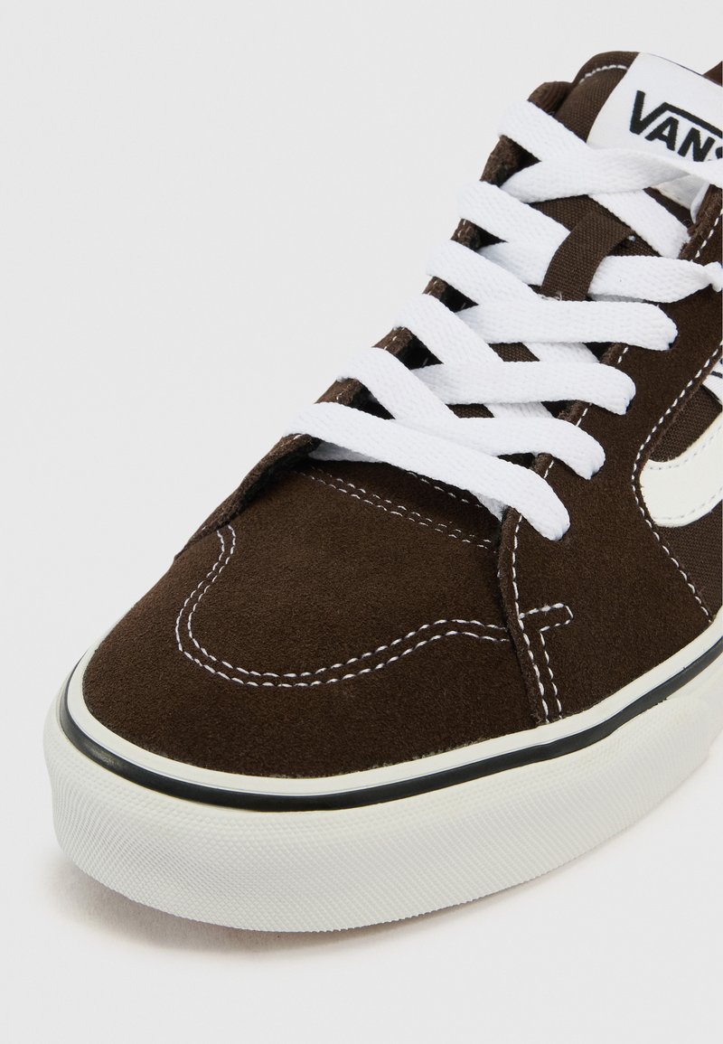 Zapatilla Vans de ante marrón con cordones blancos, franja lateral blanca, costuras blancas y una suela de goma blanca gruesa con una línea negra.