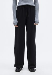 Μαύρο παντελόνι με φαρδιά μπατζάκια, ελαστική μέση και κορδόνι, κατασκευασμένο από μαλακό ύφασμα. Συνδυάζεται με γκρι, εφαρμοστό ριμπ πλεκτό πουλόβερ.