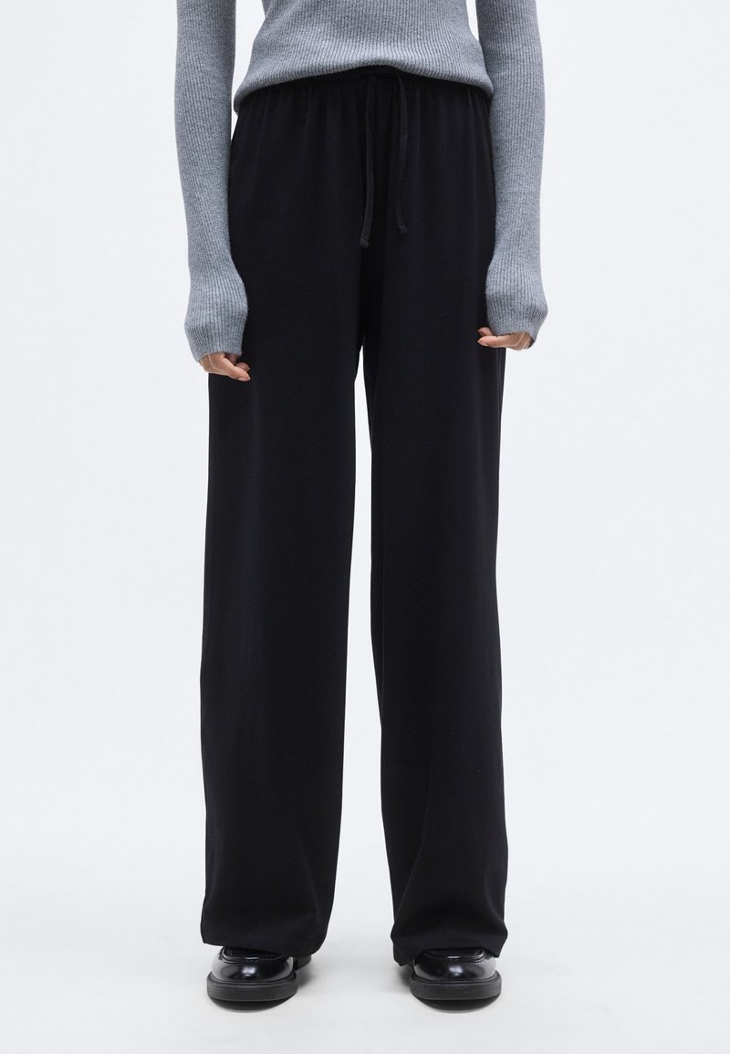 Μαύρο παντελόνι με φαρδιά μπατζάκια, ελαστική μέση και κορδόνι, κατασκευασμένο από μαλακό ύφασμα. Συνδυάζεται με γκρι, εφαρμοστό ριμπ πλεκτό πουλόβερ.