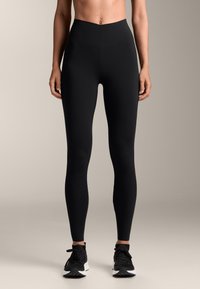 Mustat korkeavyötäröiset legginssit, jotka on valmistettu joustavasta kankaasta, jossa on sileä pinta ilman näkyviä kuvioita. Yhdistetty mustien urheilukenkiä.