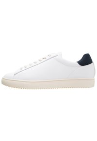 White sneaker with a smooth texture, featuring beige laces and a navy heel accent. The sole is light beige with a textured surface.