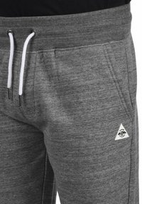 Pantalones de chándal grises, hechos de tejido suave, con cintura ajustable mediante cordón, puños acanalados y un pequeño logotipo triangular blanco en el bolsillo.