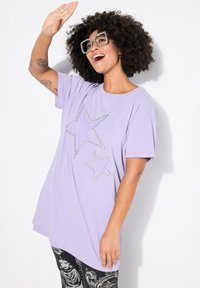 Světle fialové oversized tričko s hvězdnými designy posetými cvočky, krátkými rukávy a kulatým výstřihem, kombinované s černými legínami s potiskem.