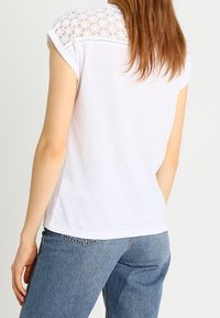 Top blanco de manga corta que presenta un diseño de encaje en los hombros, combinado con jeans de mezclilla azul clásico.