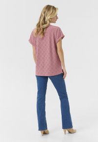 Haut rose à manches courtes avec motif en œillets, coupe décontractée et ourlet arrondi, assorti à un jean bleu évasé et des escarpins beiges.