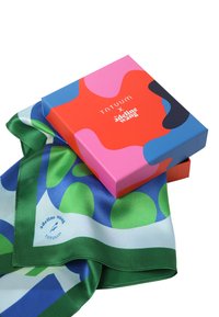 Eșarfă de mătase cu modele verzi, albastre și albe, pliată lângă o cutie colorată cu designuri abstracte roz, roșu și albastru. Textul de pe eșarfă este vizibil.