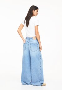 Lichtblauwe wijde spijkerbroek met een hoge taille, gemaakt van denim, met twee achterzakken en een relaxte pasvorm. Gecombineerd met een wit cropped T-shirt.