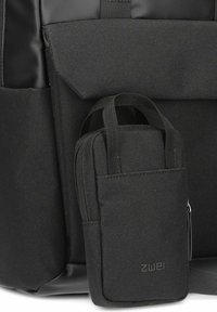Zaino nero con tessuto testurizzato, una tasca sul davanti con flap e una piccola borsa con zip staccabile con manico ad anello.