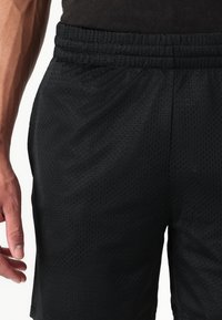 Fekete hálós sportnadrág könnyű, lélegző anyagból; elasztikus derékrésze van, és texturált, perforált felülete.