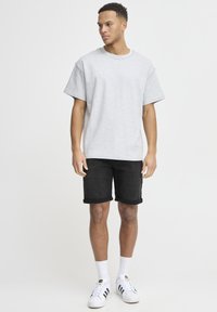 T-shirt en coton gris à manches courtes, associé à un short en denim noir. Le mannequin porte des baskets blanches avec des rayures noires et des chaussettes blanches mi-mollet.