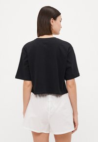 Svart kortärmad t-shirt med crew-neck, tillverkad av mjukt bomullstyg. Matchad med ljusa shorts.