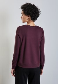 Sudadera burdeos de tejido texturizado, con cuello redondo y mangas largas, con un dobladillo inferior ajustado y un diseño minimalista.