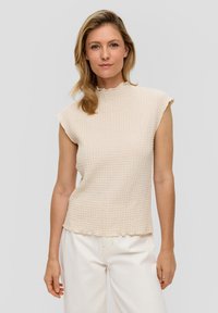Beige textuurtop met een golvende halslijn en kapmouwen, voorzien van een losse pasvorm en een subtiel wafelpatroon. Gemaakt in combinatie met lichte broeken.