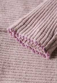 Tissu tricoté côtelé de couleur rose clair avec une surface texturée. L'ourlet présente une bordure décorative en boucle d'une teinte légèrement plus sombre de rose.