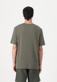 Olivgrünes T-Shirt mit kurzen Ärmeln aus Baumwolle, mit Rundhalsausschnitt und geradem Schnitt. Schlichtes Design ohne Muster oder Verzierungen.