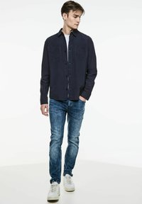 Marinblå knapp-up skjorta med två bröstfickor, kombinerat med ljusblå jeans och vita sneakers. Slätt tyg med avslappnad passform.