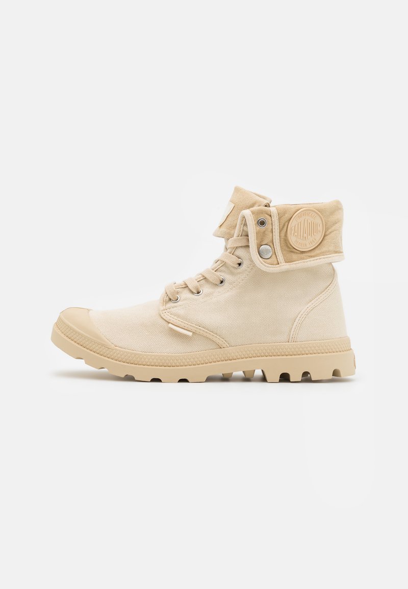 Botas de tobillo de lienzo beige con un upper texturizado, puntera de goma y un puño plegable con un parche de logo circular.